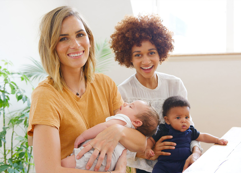 Two mothers holding their babies and smiling.