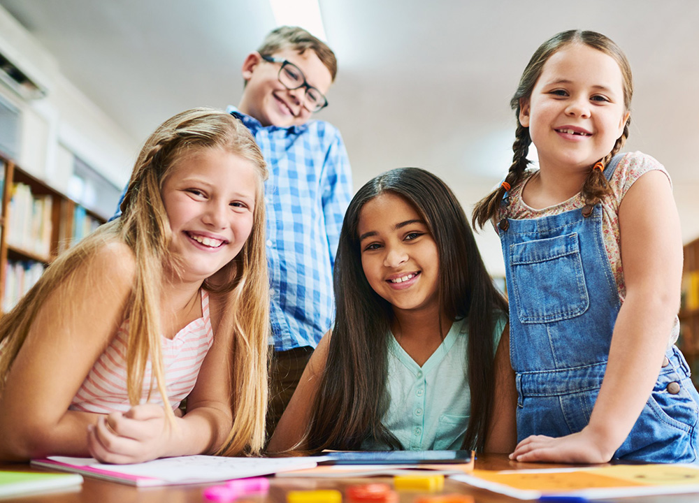 Schoolchildren sitting at a desk smiling.