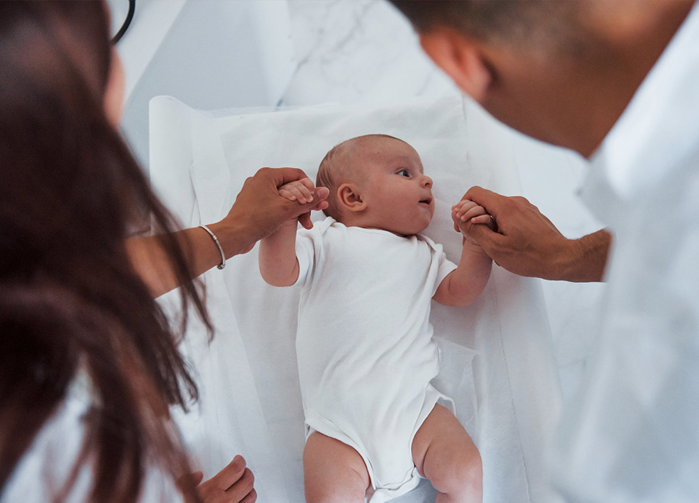 Happy parents holding the hands of their baby.